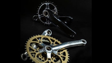 Two bicycle chainsets with gears and crank arms on a black background.