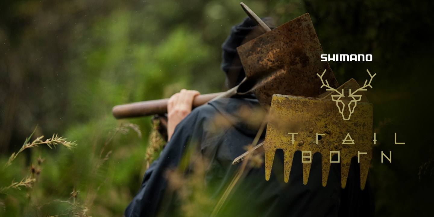 Personne portant un outil de jardinage sur l'épaule, entourée de verdure