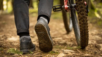 Close-up of person's shoes and mountain bike tire on a forest trail