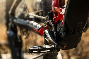 Close-up of an electric mountain bike's mid-drive motor, pedal, and chain.