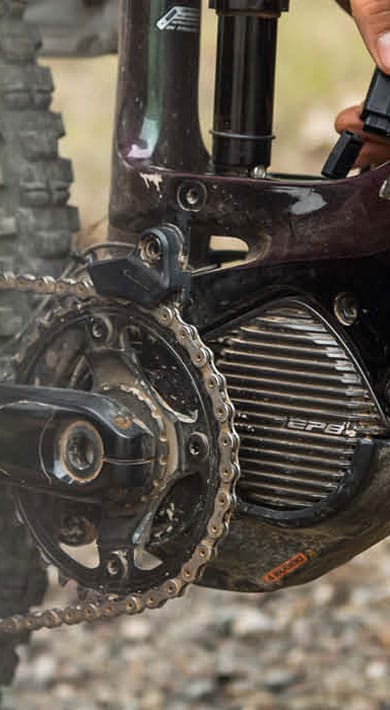 Close-up of an electric bike's mid-drive motor and chainring with a person's hands adjusting the gears.