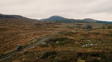 Person riding a bicycle on a path through a mountainous landscape