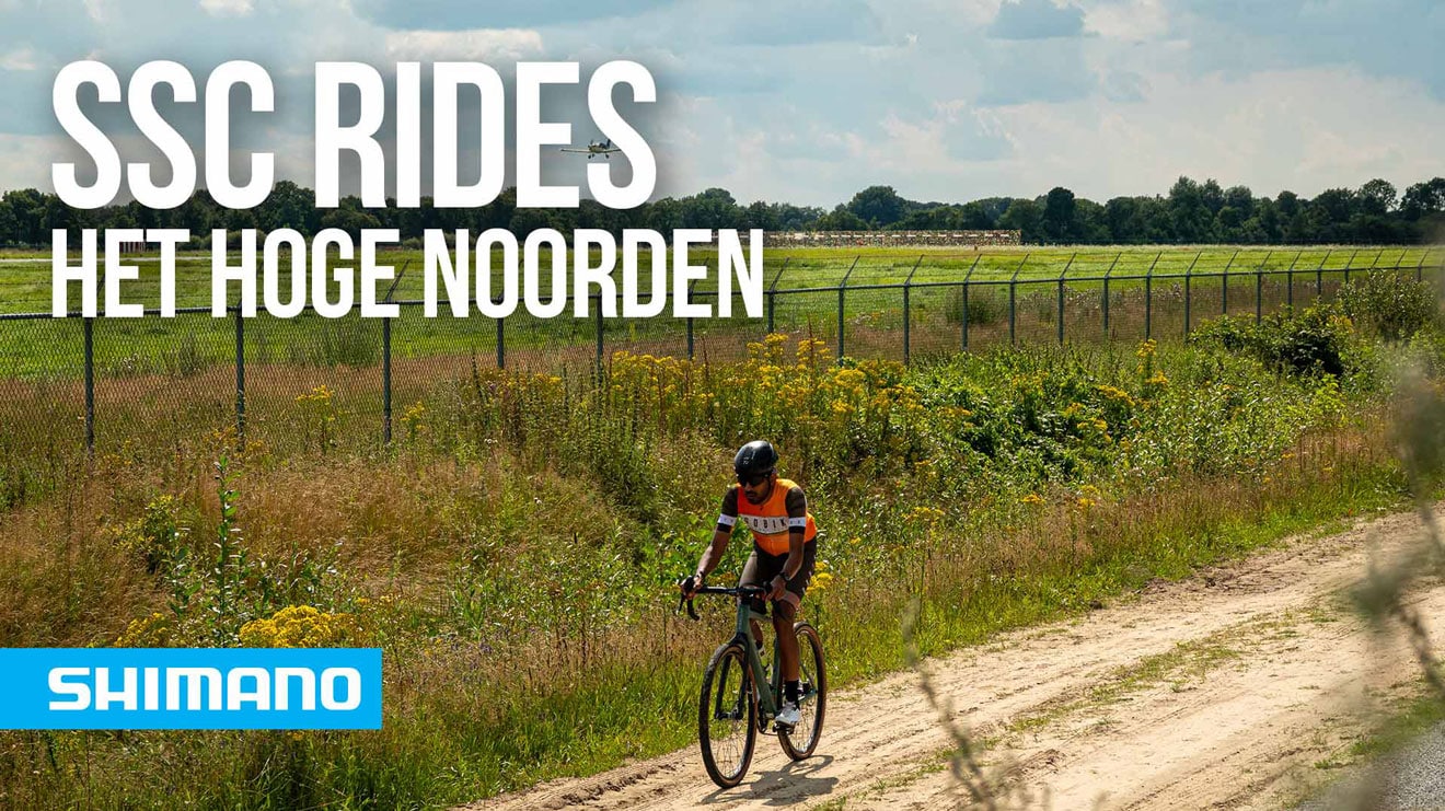 Fietser op een onverhard pad met groen en een hek op de achtergrond.