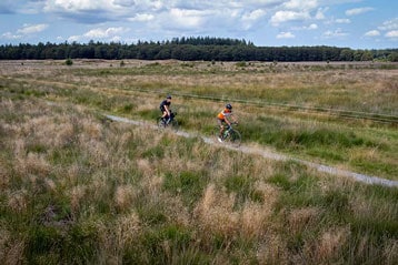 Twee fietsers rijden door een grasveld onder een deels bewolkte lucht.