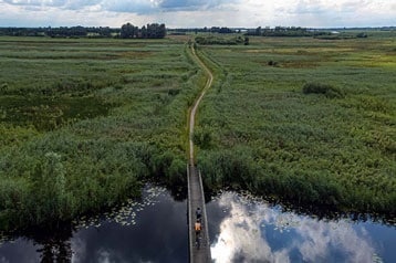 Luchtfoto van een brug over een rivier in een uitgestrekt groen landschap.