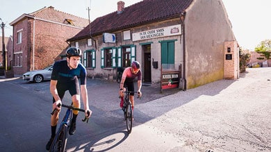 Twee fietsers rijden langs een oud gebouw op een zonnige dag.