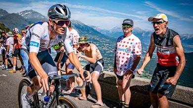 Un ciclista scala una montagna con i tifosi che festeggiano sullo sfondo