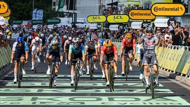 Ciclistas em sprint até à meta com o ciclista líder a celebrar a vitória numa competição lotada