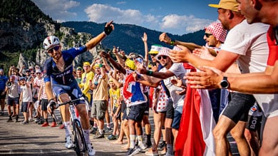 Radsportler in blauem Trikot klatscht jubelnde Zuschauer während einer Bergetappe ab