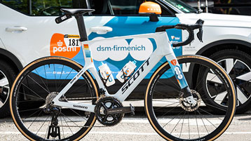 Scott racefiets met dsm-firmenich merklogo geparkeerd voor een auto.