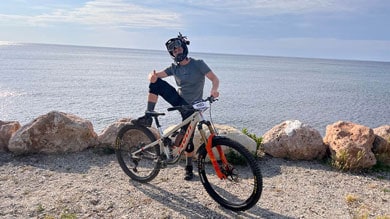 Person mit Mountainbike neben dem Meer auf einem felsigen Weg.