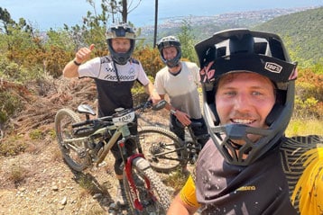 Drei Radfahrer mit Helmen posieren auf einem Trail mit einer malerischen Aussicht im Hintergrund.
