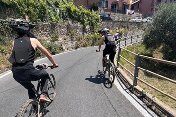 Radfahrer fahren eine malerische, enge Straße in der Nähe von Häusern hinauf.