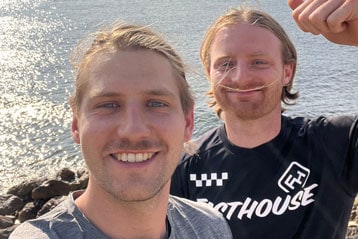 Zwei lächelnde Männer posieren für ein Selfie am Meer.