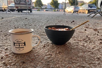 Kaffeetasse und Schale mit Müsli und Löffel auf dem Gehweg.