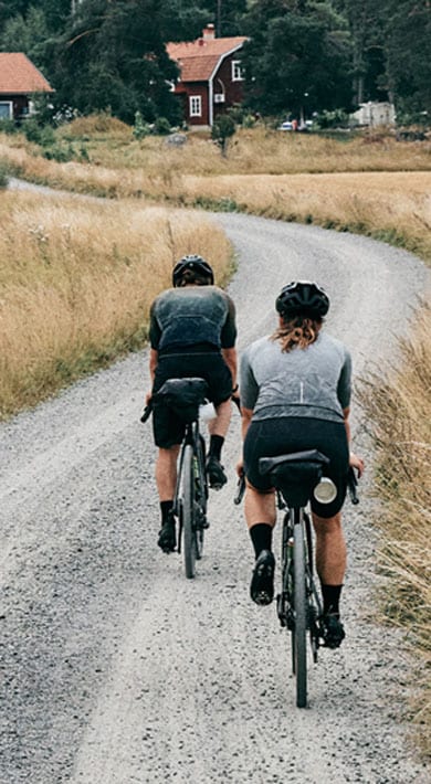 Three cyclists riding on a gravel road through a rural landscape with fields and trees.