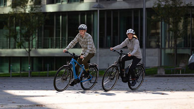Zwei Personen fahren mit Helmen Fahrrad in einem städtischen Gebiet.