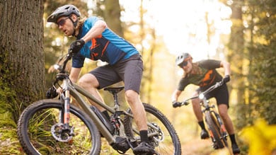 Zwei Mountainbiker fahren auf einem Waldweg.