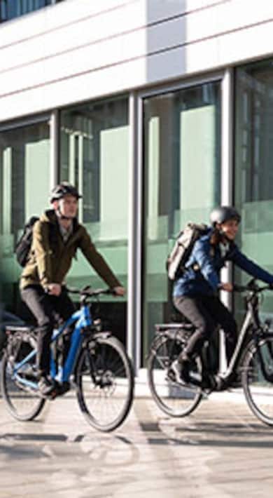 Zwei Radfahrer fahren an einem modernen Gebäude mit Glasfenstern vorbei.