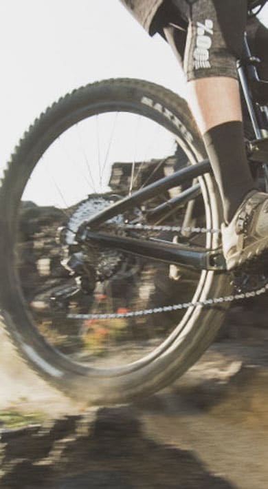Mountainbiker fährt auf einem felsigen Trail mit Bäumen und Hügeln im Hintergrund.
