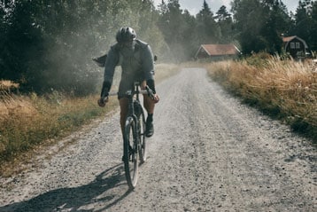 Cyclist riding on a gravel road with trees and houses in the background