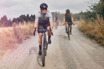 Cyclists riding on a gravel road surrounded by fields and trees