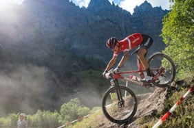 Mountain biker racing downhill on a trail with mountains in the background