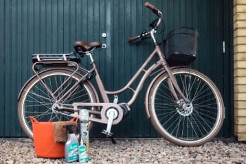 Vintage bicycle with basket near cleaning supplies and a tool bag in front of a green garage door