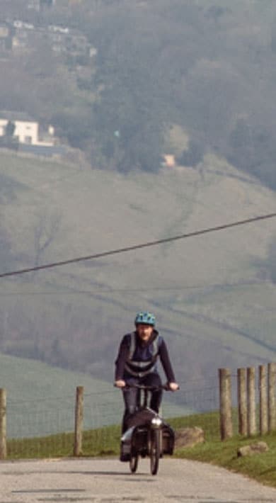 Person riding a bicycle on a rural road with rolling hills in the background