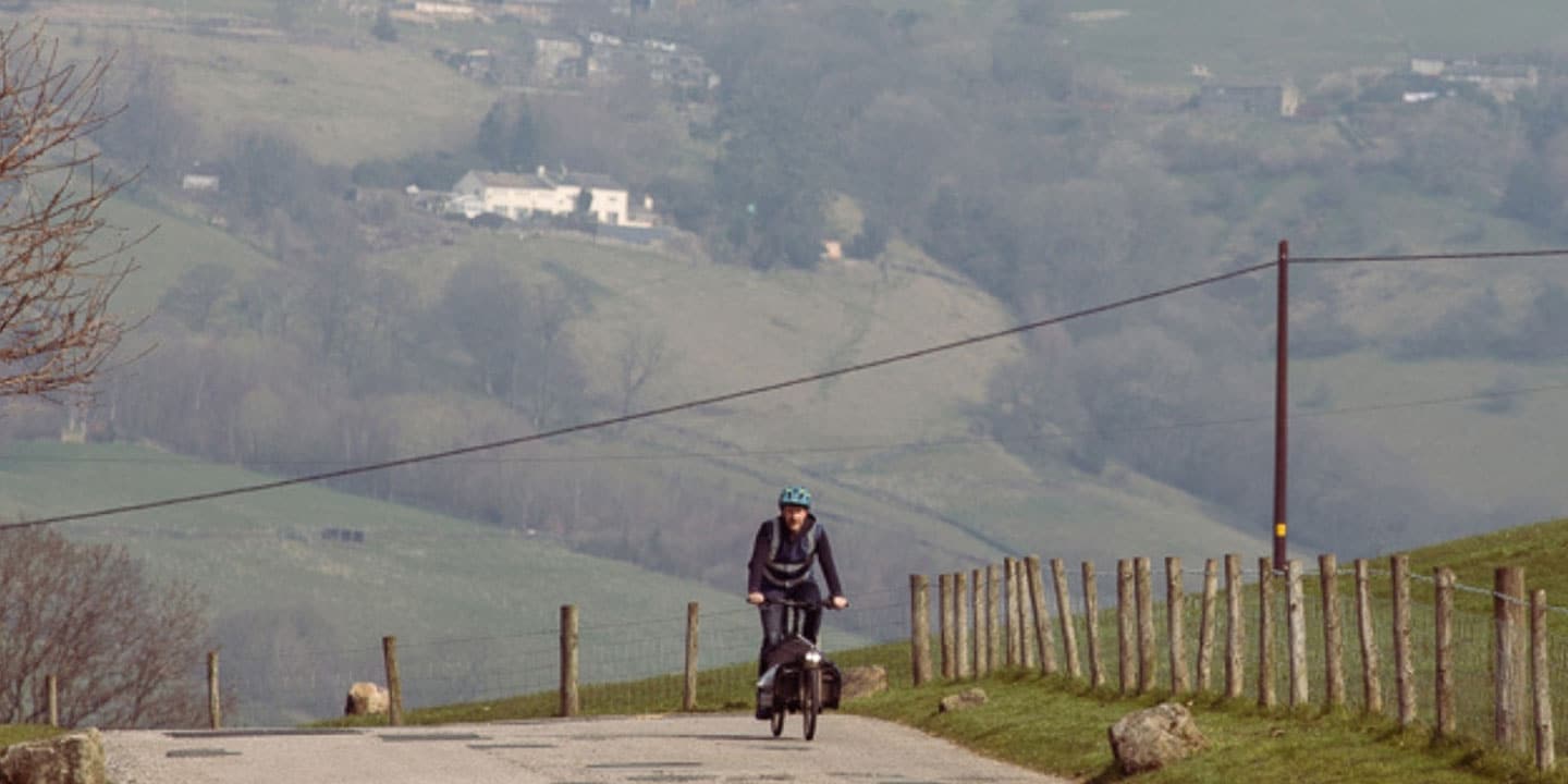 Person riding a bicycle on a rural road with rolling hills in the background