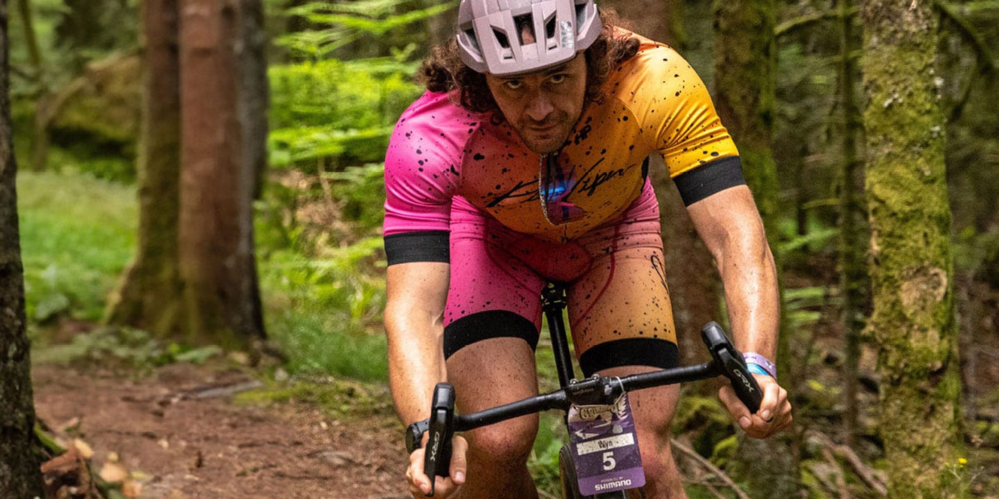 Cyclist in a pink and yellow outfit riding through a dense forest trail