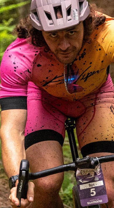 Cyclist in a pink and yellow outfit riding through a dense forest trail