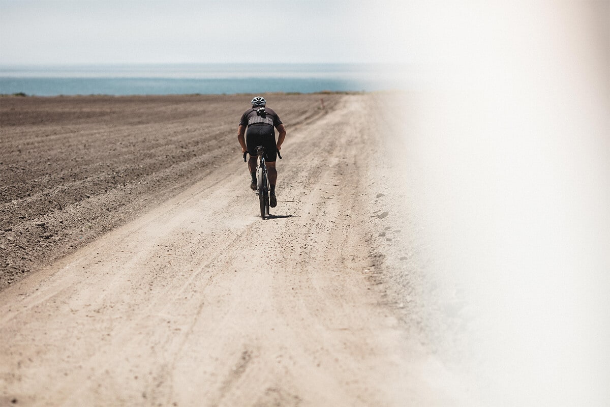Gravel Cyclist riding down a dirt road in the desert with camera on his back